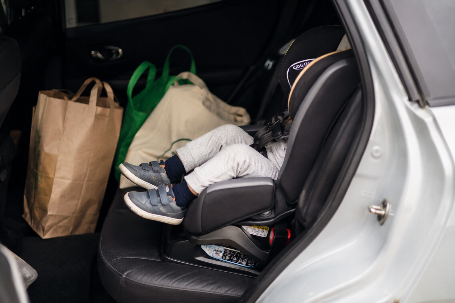 Toddler's shoes and legs in a car seat, grocery bags visible, real errands-day scene