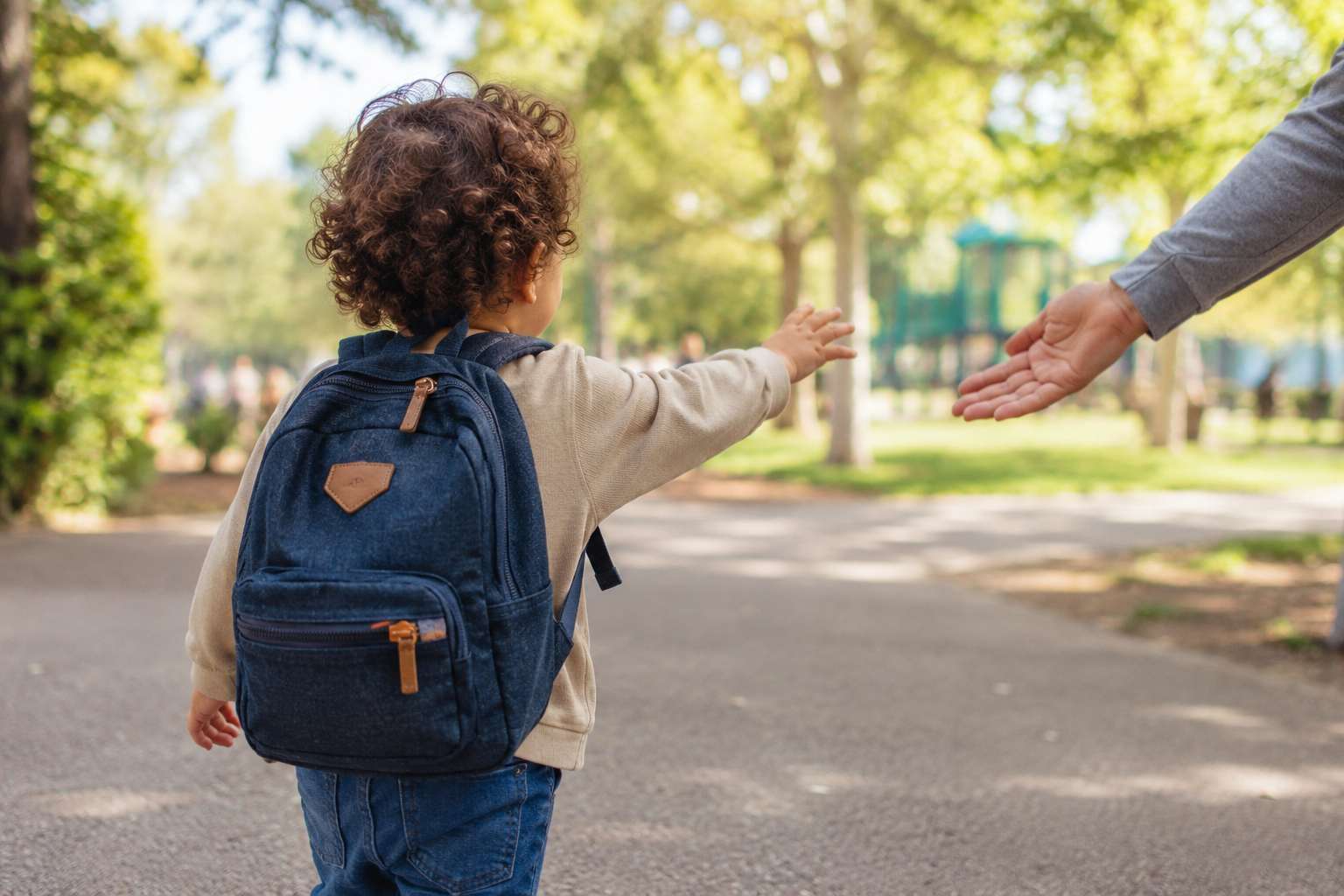 Toddler's back and small backpack walking toward a park, mid-morning light