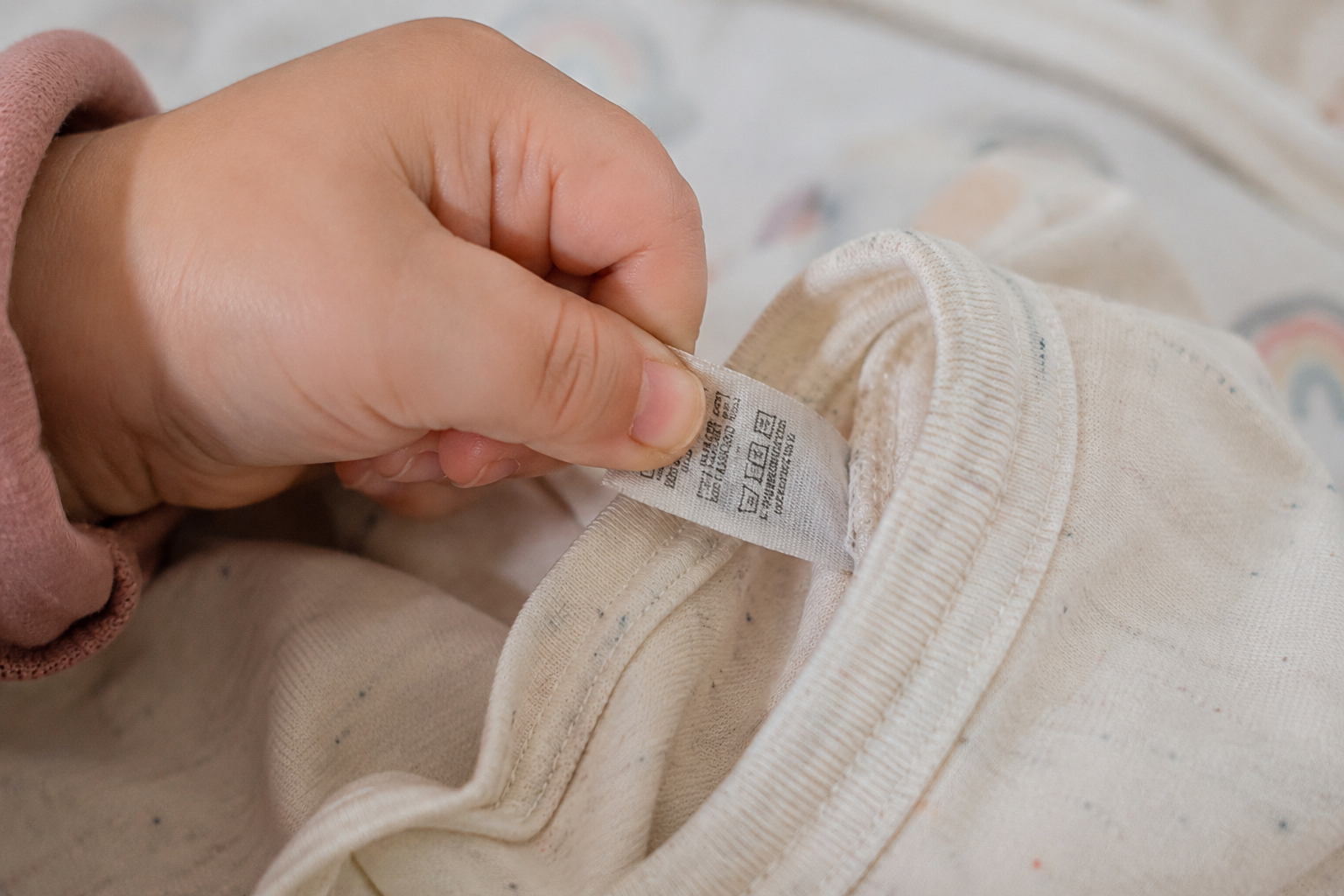 Close-up of a toddler's hand pulling at a clothing tag inside a shirt collar