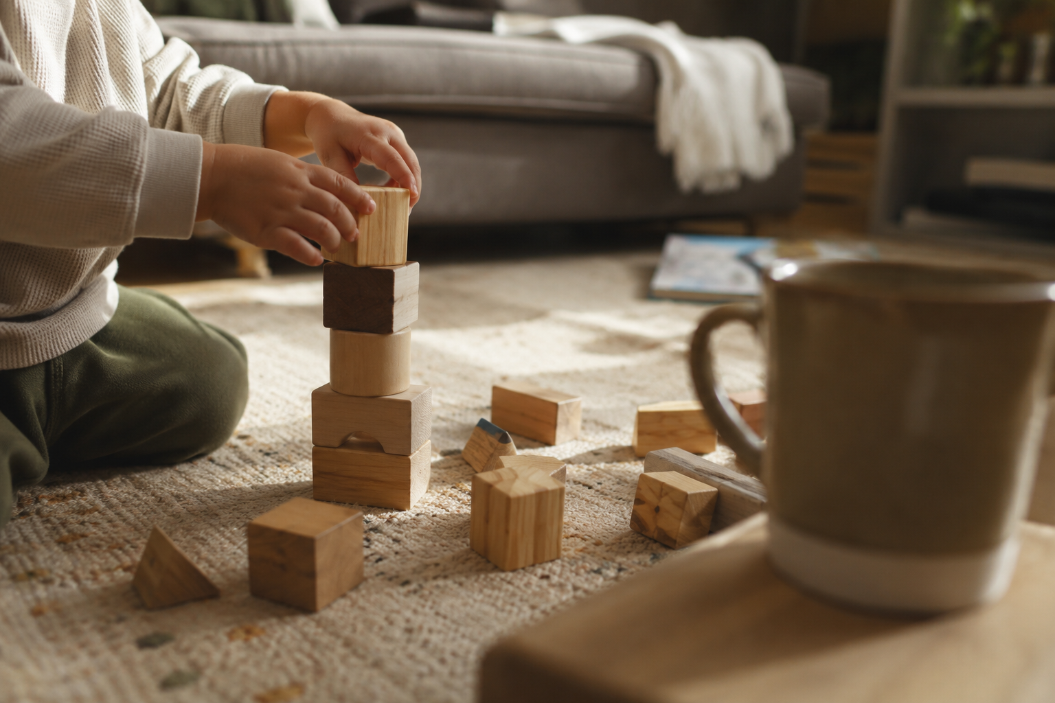 Toddler's hands building with blocks on a living room rug, soft weekend morning light, no rush